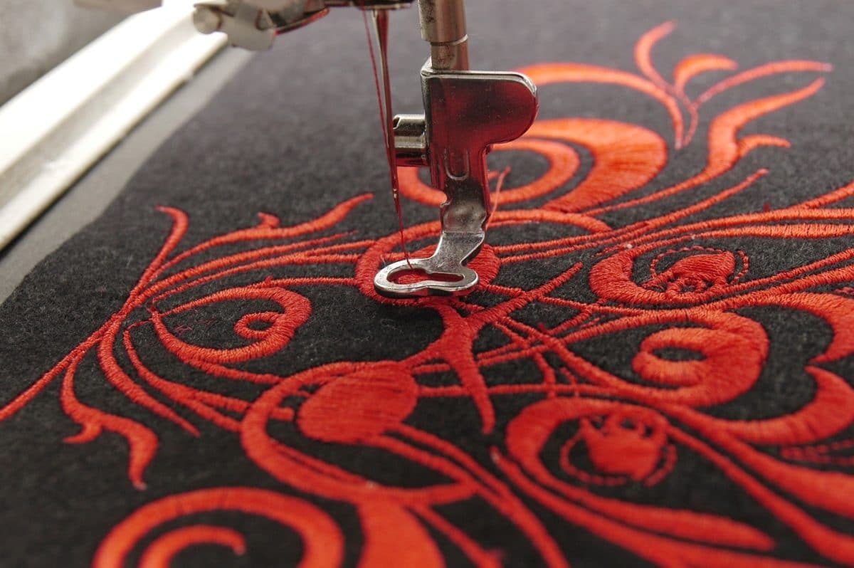 A beginner sewing machine embroidering a red pattern into a piece of black fabric 